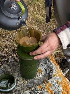 a person pours water into a cup from a coffee maker in the wilderness,