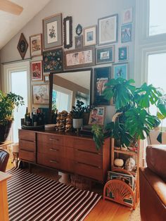 a living room filled with lots of pictures and plants on the wall next to a dresser