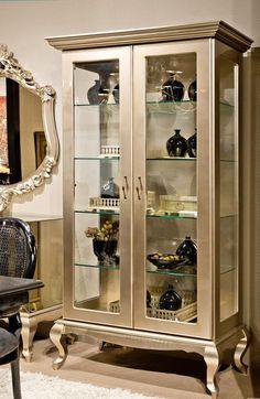 a glass door cabinet in a room with a mirror on the wall and a black chair next to it