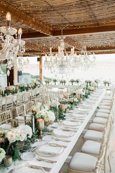 a long table is set up with white flowers and greenery for an elegant wedding reception