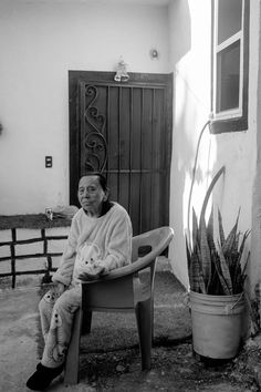 an old woman sitting in a chair next to a potted plant and a door