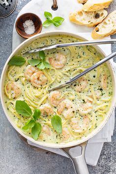 pasta with shrimp and pesto in a skillet next to bread on a table