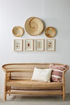 a wicker couch with pillows on it in front of three framed pictures and two wall hangings