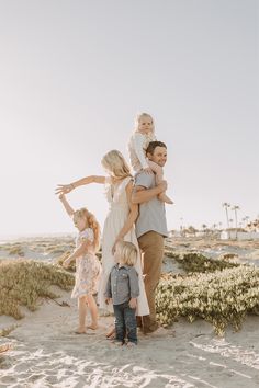 a family standing in the sand at the beach with their arms around each other and one child