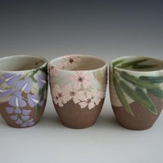 three vases with flowers painted on them sitting next to each other