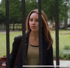 a young woman standing behind bars in front of a building with trees and grass on the other side