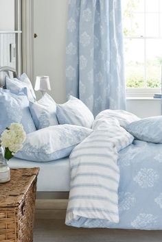 a bed with blue and white comforters in a bedroom next to a window filled with flowers