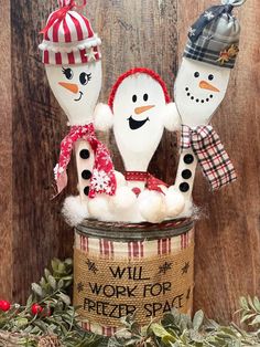 three snowmen are sitting in a tin with christmas decorations on it and one is wearing a hat