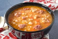 a black bowl filled with soup on top of a red and white napkin next to a spoon