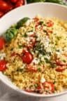 a white bowl filled with rice and vegetables on top of a table next to tomatoes