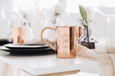 a rose gold coffee mug sitting on a table next to some candles and other decorations