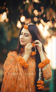 a woman in an orange outfit with flowers around her neck and hands on her head