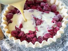 a bowl filled with raspberries and cream being drizzled