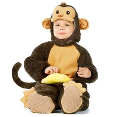 a baby in a monkey costume sitting on the ground with a banana and wearing a hat