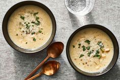 two bowls of soup with spoons next to each other on a silver tablecloth