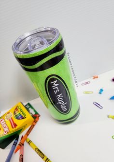 there is a green cup with writing on it next to crayons and pencils