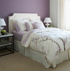 a bed with white and purple comforters in a bedroom next to two lamps on either side of the bed