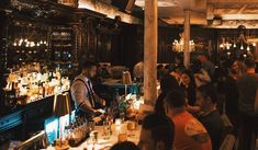 a group of people sitting at a bar with bottles on the counter and lights hanging from the ceiling