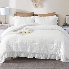 a bed with white comforter and pillows on top of it next to a night stand