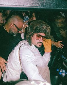 a man wearing a fur hat and sunglasses sitting in front of a group of people