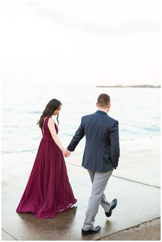 a man and woman holding hands walking by the water