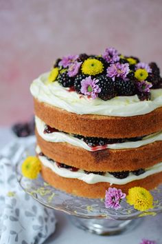 a cake with white frosting and fresh berries on top is sitting on a glass plate