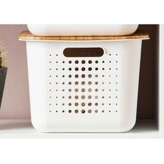 a white plastic basket with a wooden lid on top of a shelf next to a potted plant