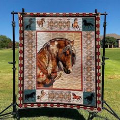 a quilt with a horse on it sitting in the grass next to a metal stand