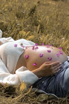 a pregnant woman laying in the grass with pink flowers on her stomach and belly,