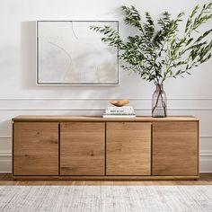 a living room with white walls, wooden furniture and a plant on the sideboard