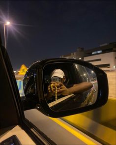 a man taking a photo in the side mirror of a car at night with his cell phone