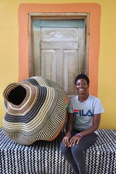 a woman sitting on top of a couch next to a large woven bag and hat