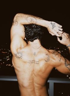 the back of a man with tattoos on his upper and lower half, standing in front of a cityscape