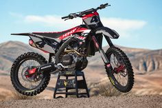 a red and black dirt bike sitting on top of a metal stand in the desert