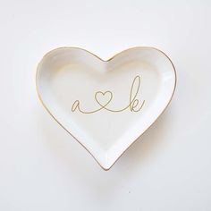 a heart shaped dish with the word love written in gold ink on it's side