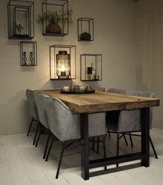 a dining room table with chairs and lights on the wall above it, surrounded by hanging planters