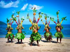 some people are standing on the beach with their arms in the air and wearing costumes