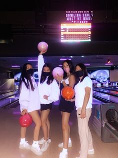 four girls in white shirts and black shorts are holding bowling balls while posing for the camera