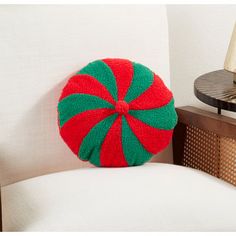 a red and green pillow sitting on top of a white chair next to a lamp