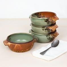 four ceramic bowls with spoons are stacked on top of each other in front of a napkin