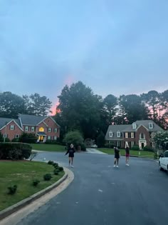 two people are walking down the street in front of some houses at sunset or dawn