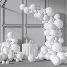 white balloons are floating in the air next to a table with a vase on it