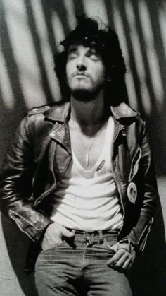 a black and white photo of a man in a leather jacket leaning against a wall