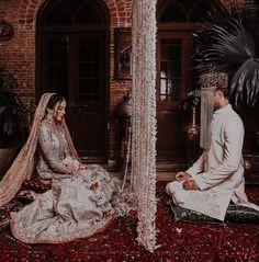 a bride and groom sitting on the ground in front of a building with red petals