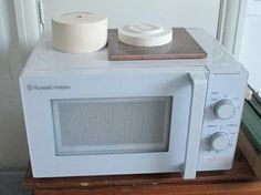 a white microwave oven sitting on top of a wooden table next to a roll of toilet paper