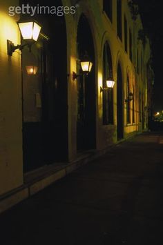 an empty street at night with lights on the buildings and windows lit up by lamps