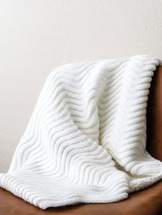 a white knitted blanket sitting on top of a brown leather chair next to a wall