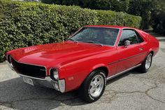 a red car parked in front of a hedge