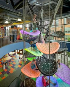 children are playing in an indoor play area with colorful mats and climbing ropes on the walls