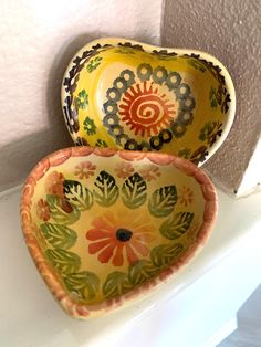 two colorful bowls sitting on top of a white counter next to each other in front of a wall